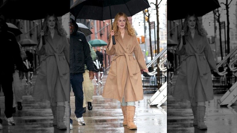 Nicole Kidman on set of "Babygirl," wearing a tan trench coat, tall UGGs, jeans, and holding an umbrella