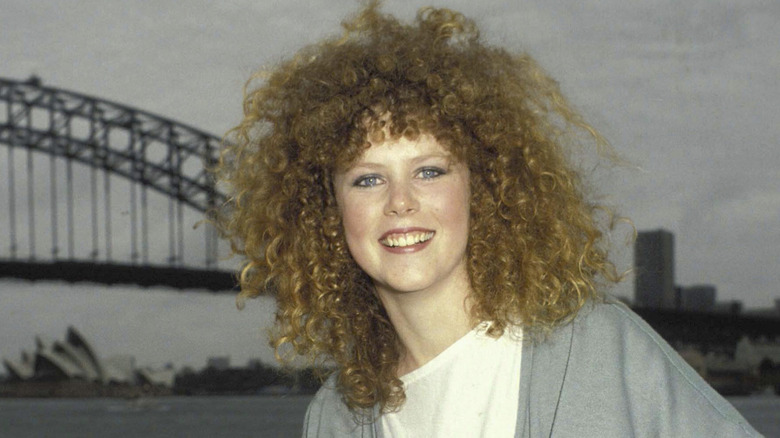 Nicole Kidman with natural curly hair smiling in front of bridge