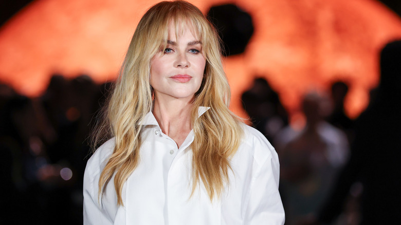 Nicole Kidman in a white collared shirt and a long-haired wig.