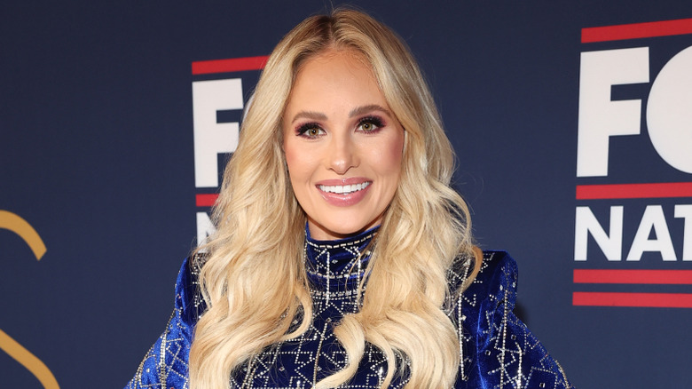 Tomi Lahren smiling in a blue dress with her hands on her hips.
