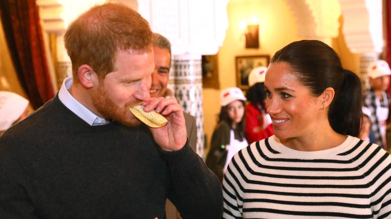 Prince Harry eating something while Meghan Markle watches