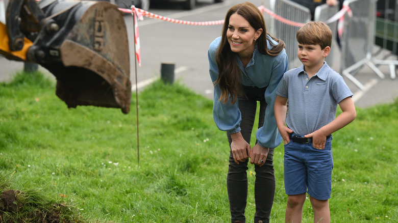 Prince Louis and Princess Catherine standing on grass looking at a digger