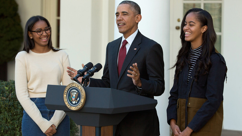 Barack Obama flanked by Sasha Obama and Malia Obama as he delivers a speech behind a podium