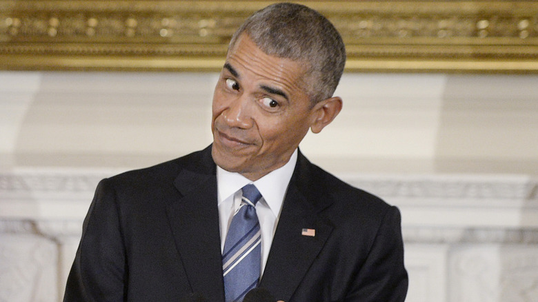 Barack Obama looking mischievous in a black suit with a blue tie