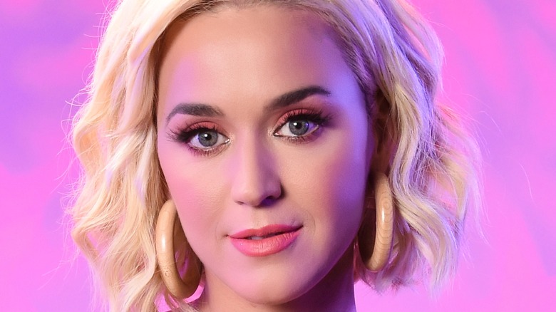 Katy Perry softly smiling against a purple and pink background