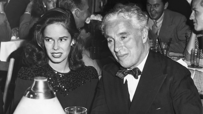 Charlie Chaplin and Oona O'Neill smiling at a dinner table.