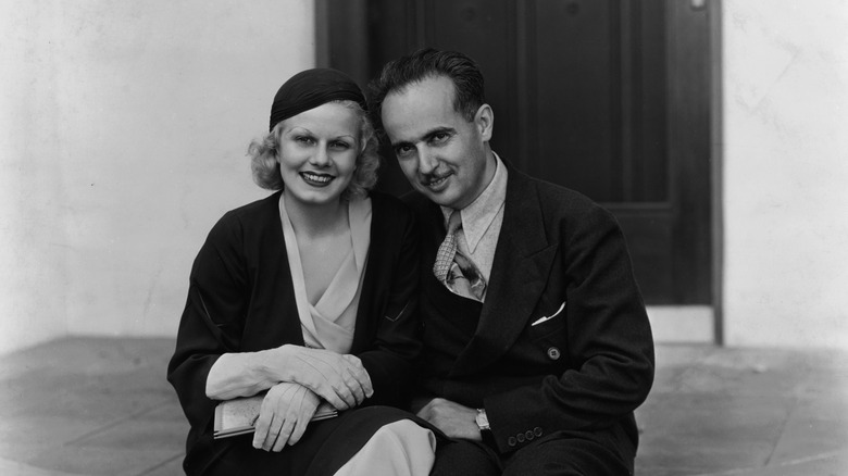 Jean Harlow and Paul Bern sitting and smiling in dark formals.