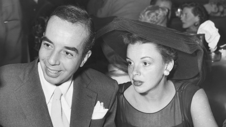 Judy Garland in a hat sitting beside a smiling Vincente Minnelli.