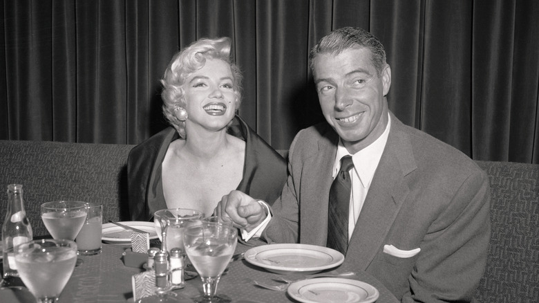 Marilyn Monroe and Joe DiMaggio sitting at a dinner table smiling.