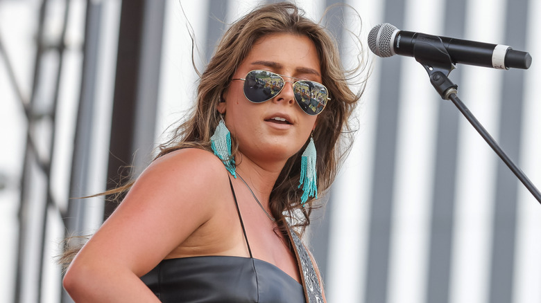 Ella Langley in Aviator sunglasses and turquoise beaded earrings playing guitar onstage