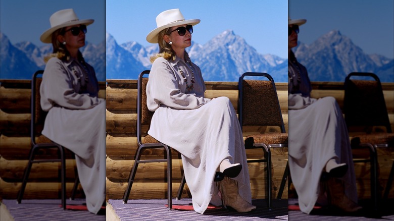 Hillary Clinton sits on a chair wearing a gray dress and rancher hat