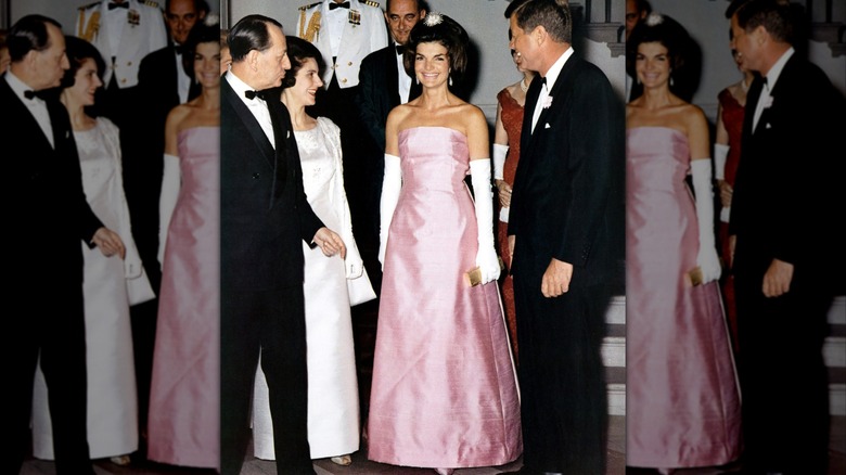 Jacqueline Kennedy Onassis smiles while wearing a pink formal dress and opera gloves
