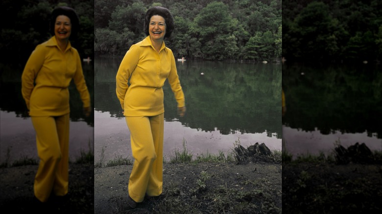 Lady Bird Johnson laughs while wearing a yellow shirt and slacks