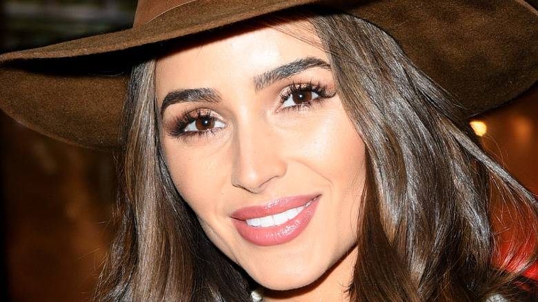 Olivia Culpo smiles in a brown hat