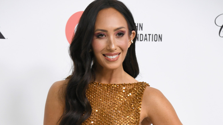Cheryl Burke in a boat-necked sequined mesh dress posing for the cameras on the red carpet