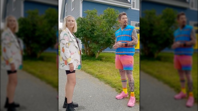 David Bromstad wearing multicolored shirt, shorts, and sneakers, standing with a 'My Lottery Dream Home' winner