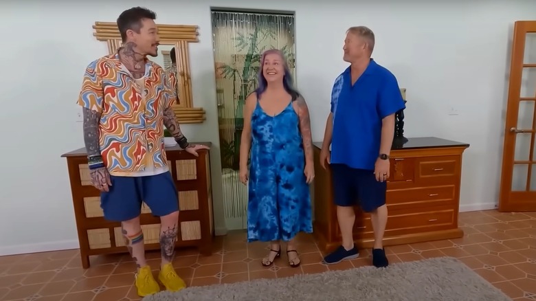 David Bromstad wearing a wavy pattern shirt yellow sneakers, standing with two 'My Lottery Dream Home' winners