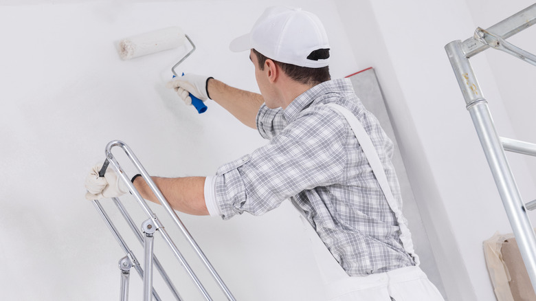 Man standing on a ladder with a paint roller in his hand.