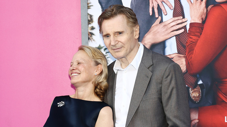 Pamela Anderson smiling and leaning against a smiling Liam Neeson