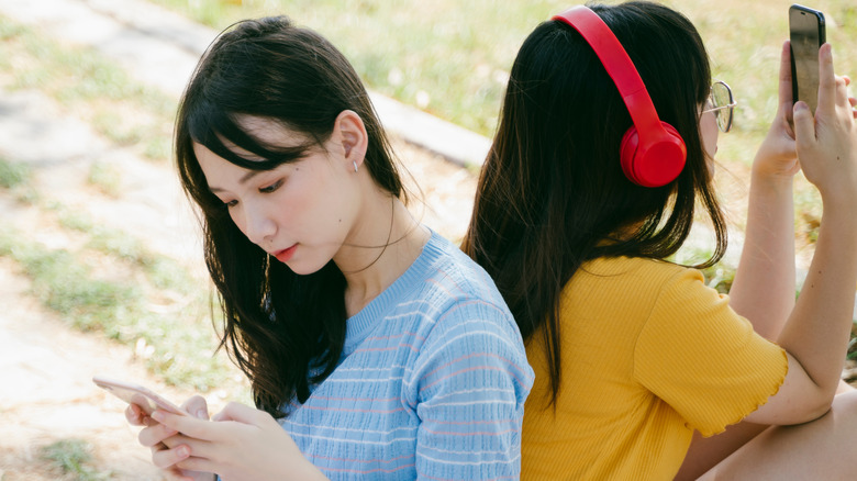 friends sitting back to back on phones