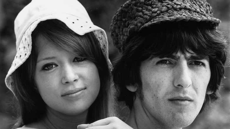 Pattie Boyd in a bucket hat holding onto George Harrison in a woven cap on their honeymoon in