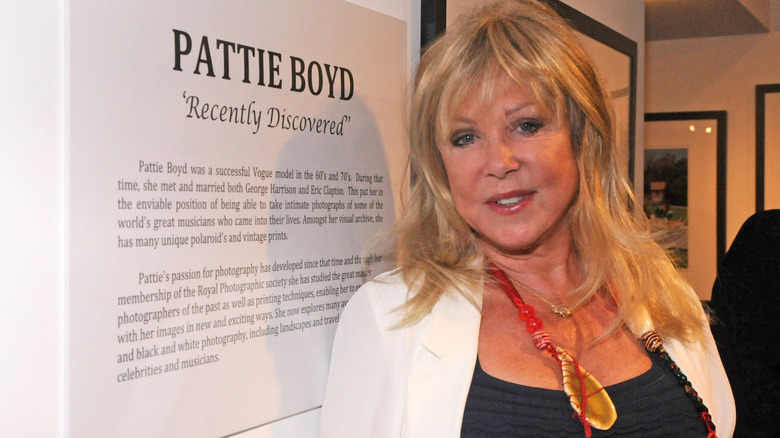 Pattie Boyd smiling by a sign at an exhibit about her.