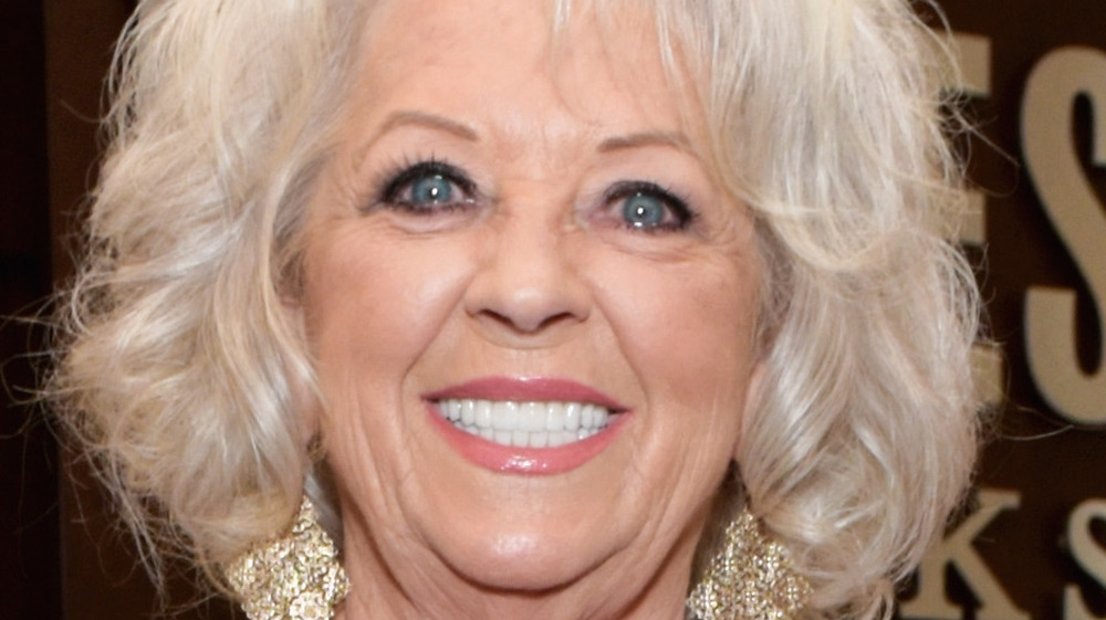 Paula Deen smiles with large gold earrings.