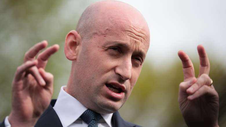 Stephen Miller making air quotes as he speaks in a black suit