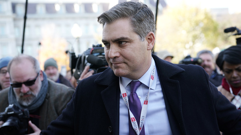 Jim Acosta walking in a suit surrounded by other reporters