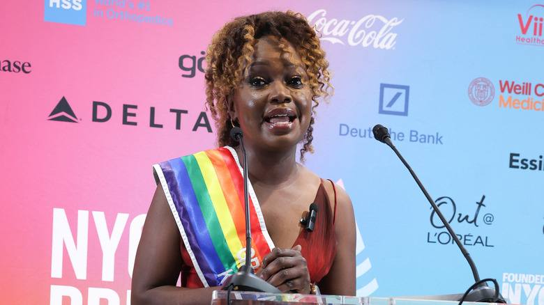 Karine Jean-Pierre giving a speech draped in a rainbow sash