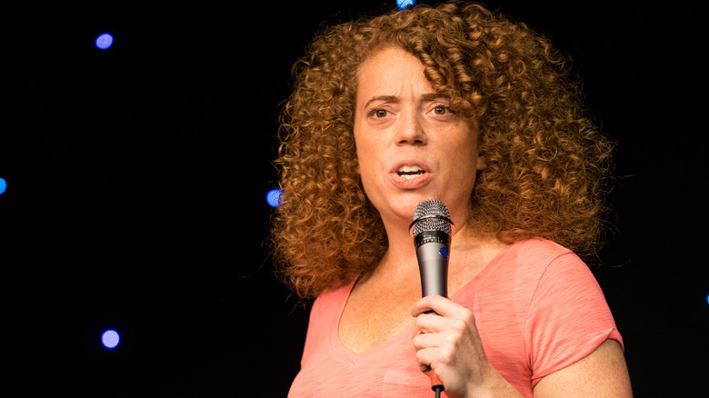 Michelle Wolf performing onstage in an orange T-shirt