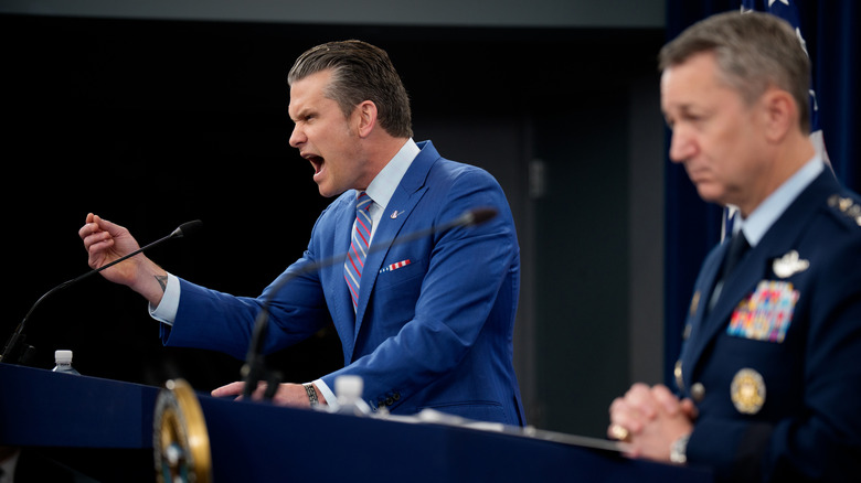 Pete Hegseth gesturing with his hand mid-outburst at podium during Pentagon briefing while Air Force Gen. Dan Caine stands next to him