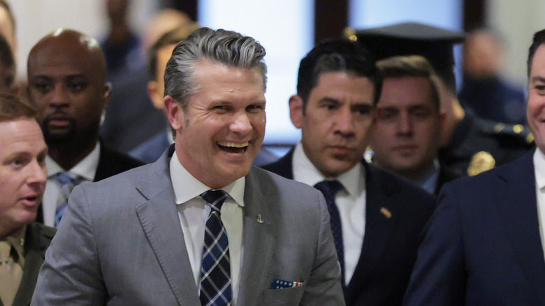 Pete Hegseth grinning and laughing while Chief of Staff Rick Buria looks seriously from behind him