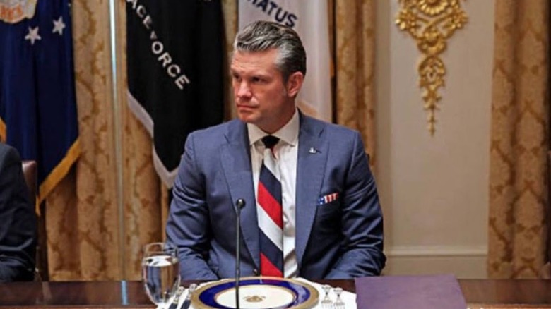 Pete Hegseth looking serious and sitting at a table