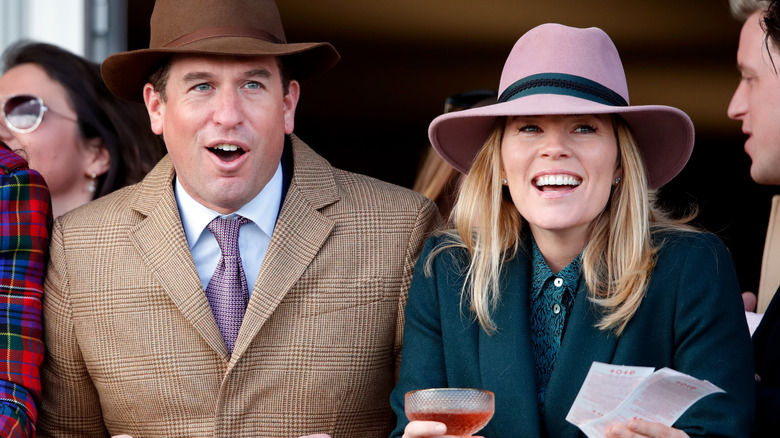 Peter Phillips looks amused next to Autumn Kelly smiling in a pink hat