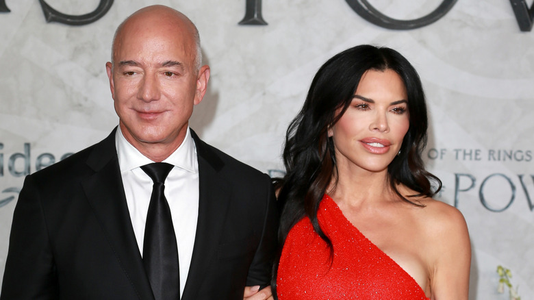 Lauren Sanchez is wearing a red dress while her hand is wrapped around Jeff Bezos' arm while he's wearing a suit.