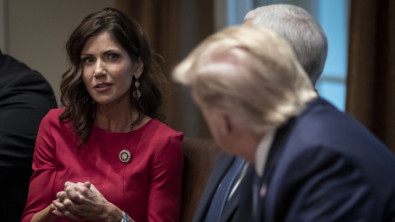 Kristi Noem sitting among three men, talking to President Donald Trump.