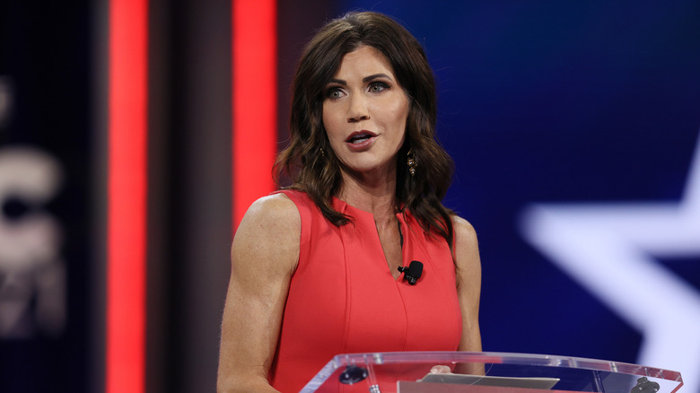 Kristi Noem behind a glass podium in a red dress.