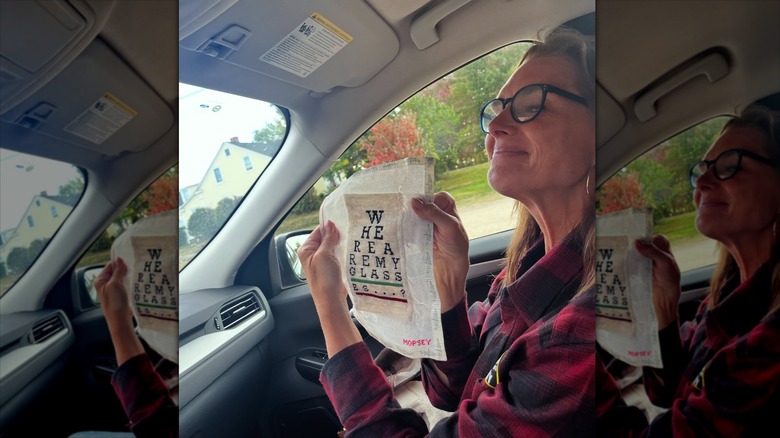 Brooke Shields in the passenger seat of a car, holding up an embroidery.