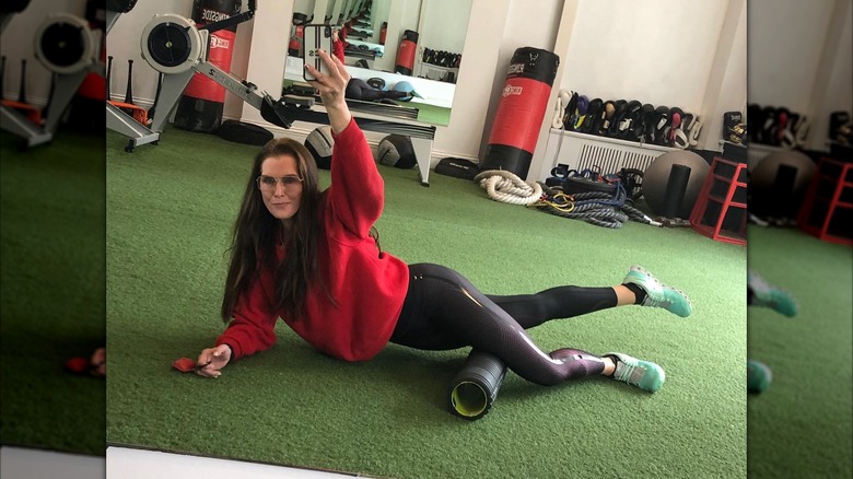 Brooke Shields laying on the ground in a gym, taking a selfie in the mirror