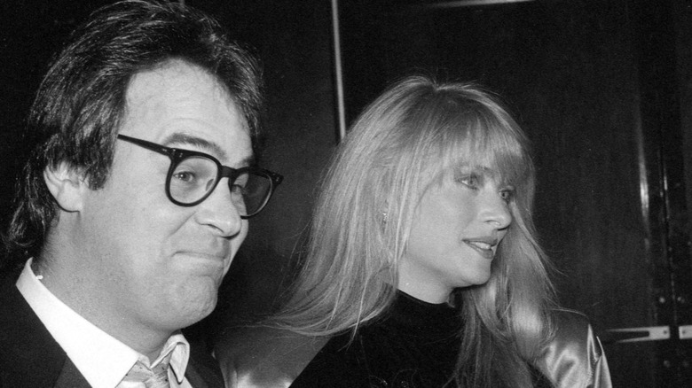 Dan Aykroyd smiles for the camera as his wife, Donna Dixon looks off to the side.