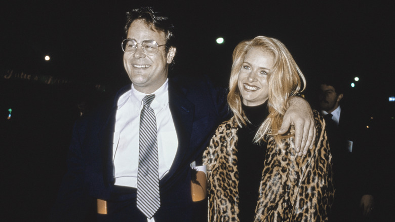 Dan Aykroyd, wearing a black blazer over a white shirt with a diagonally striped tie, his left arm around his wife, American actress Donna Dixon, who wears a leopard-skin coat over a black turtleneck outfit, attend the Westwood premiere of 'Empire of the Sun,' at the Mann Village Theater in the Westwood neighbourhood of Los Angeles, California, 8th December 1987.