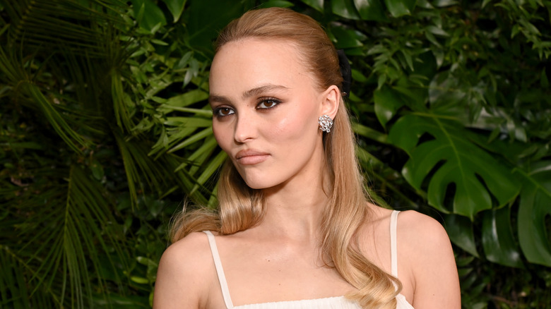 Lily-Rose Depp in white dress against a leafy background
