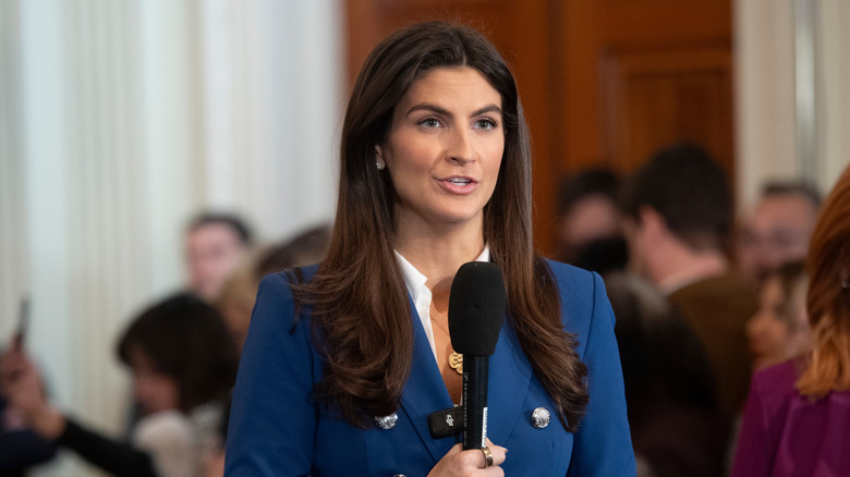 Kaitlan Collins holding a microphone while asking questions at the White House