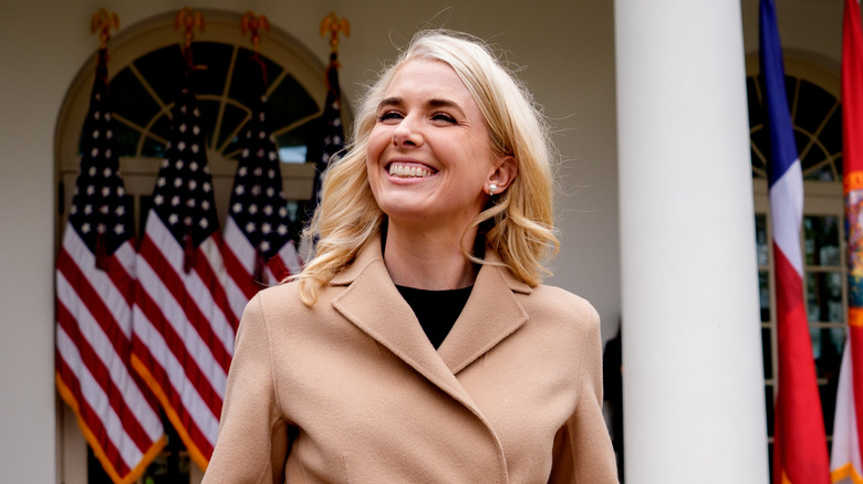 Natalie Harp with a big grin on her face in a camel coat with American flags behind her