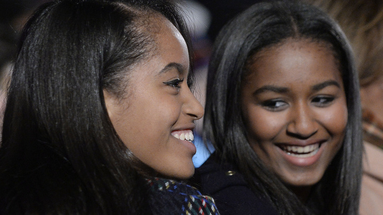 Malia Obama looking straight ahead with Sasha Obama to her side, looking at her older sister.