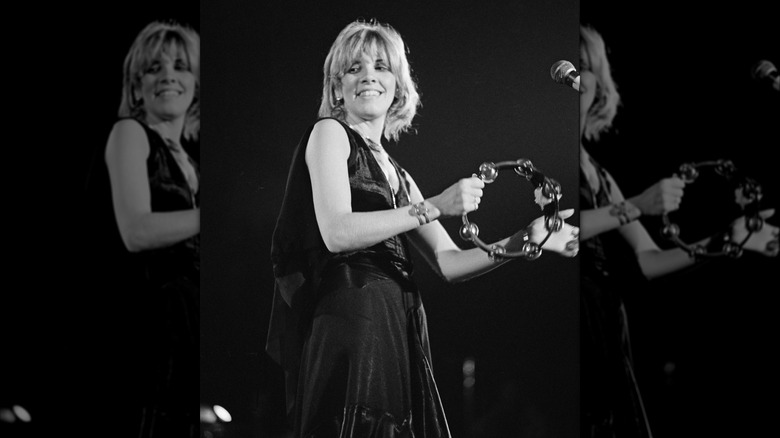 Stevie Nicks performing in 1975 wearing a black sleeveless dress and playing her tambourine