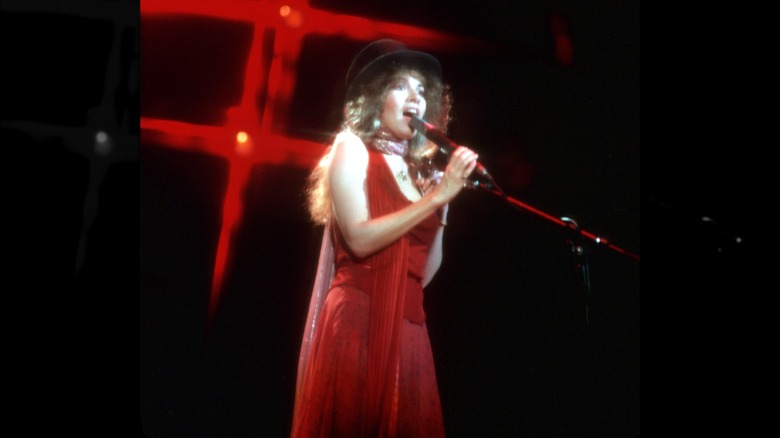 Singer Stevie Nicks performing in December 1979 while wearing a red dress, black top hat, and skinny scarf