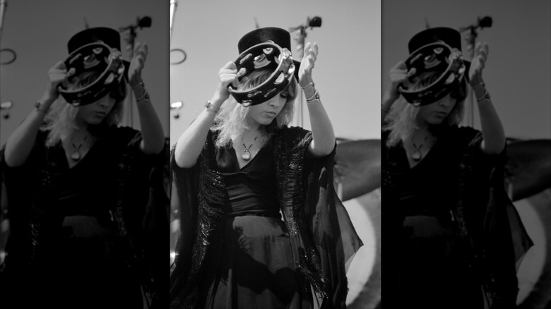 Black and white photo Stevie Nicks performing with Fleetwood Mac in 1976 wearing a black dress and a top hat, playing a tambourine