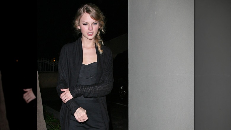 Taylor Swift in all black, holding her arm and looking down at the ground.